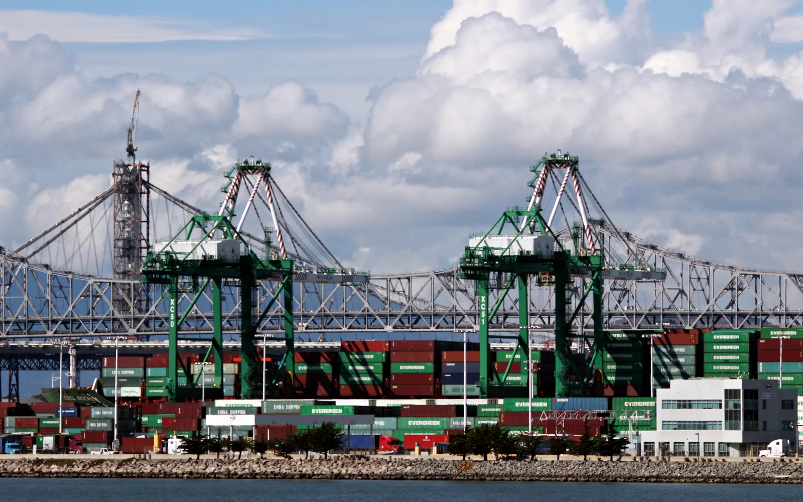Port of Oakland container cranes and cargo operations with dramatic cloudy sky